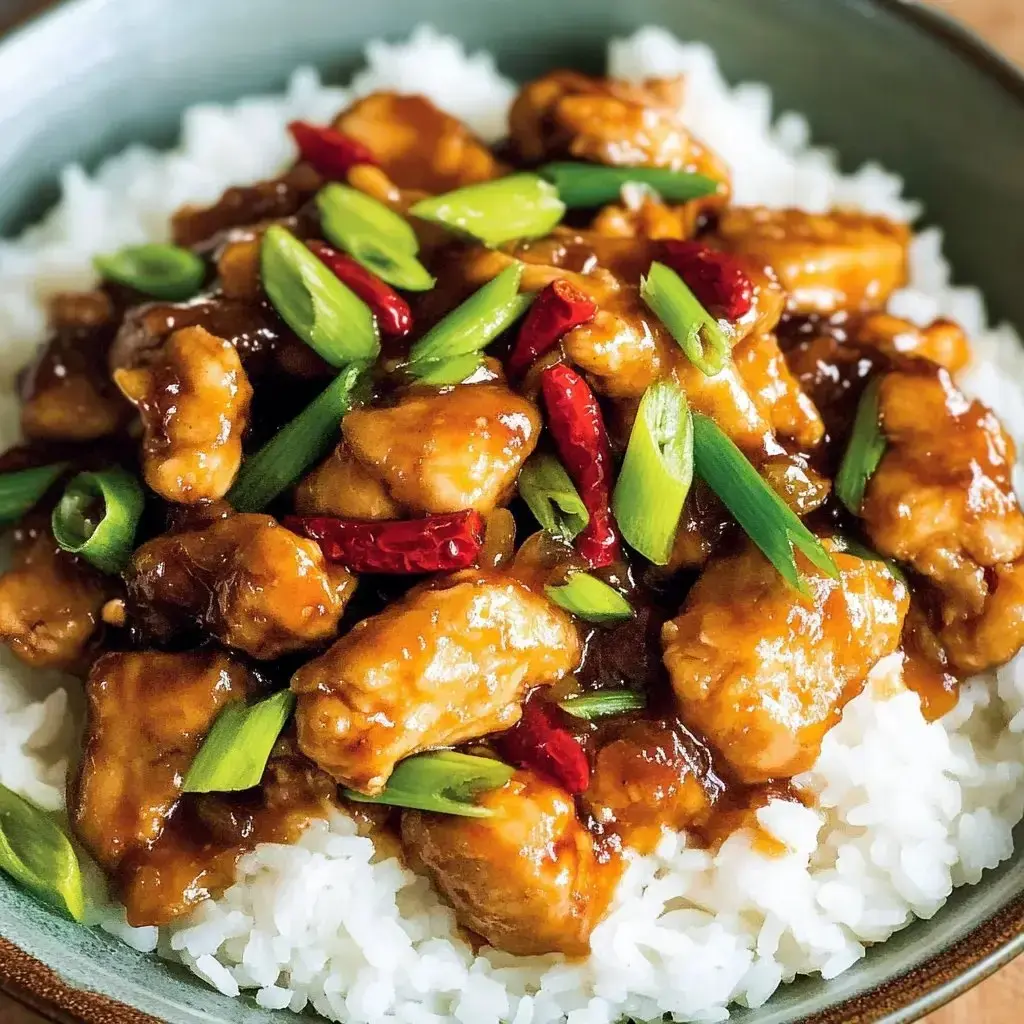 A plate of saucy chicken over rice, sprinkled with green onions and dried chili peppers.