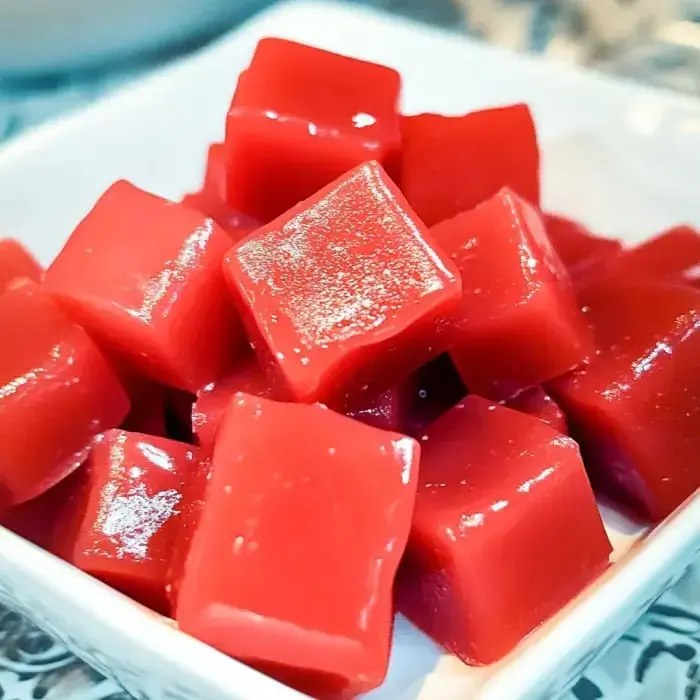 Shiny red candy squares stacked in a white dish, close-up view.