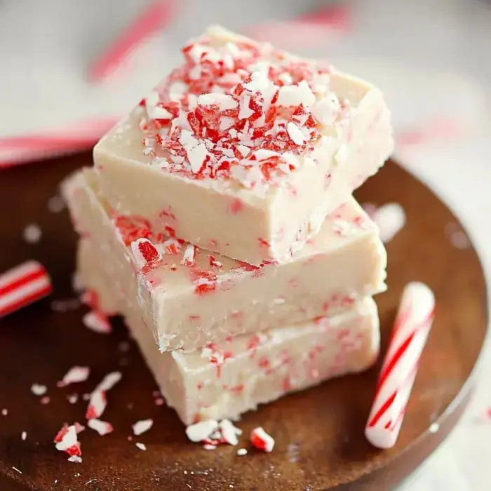 Soft white peppermint fudge topped with crushed candy canes, placed alongside little candy cane decorations on a wooden board.