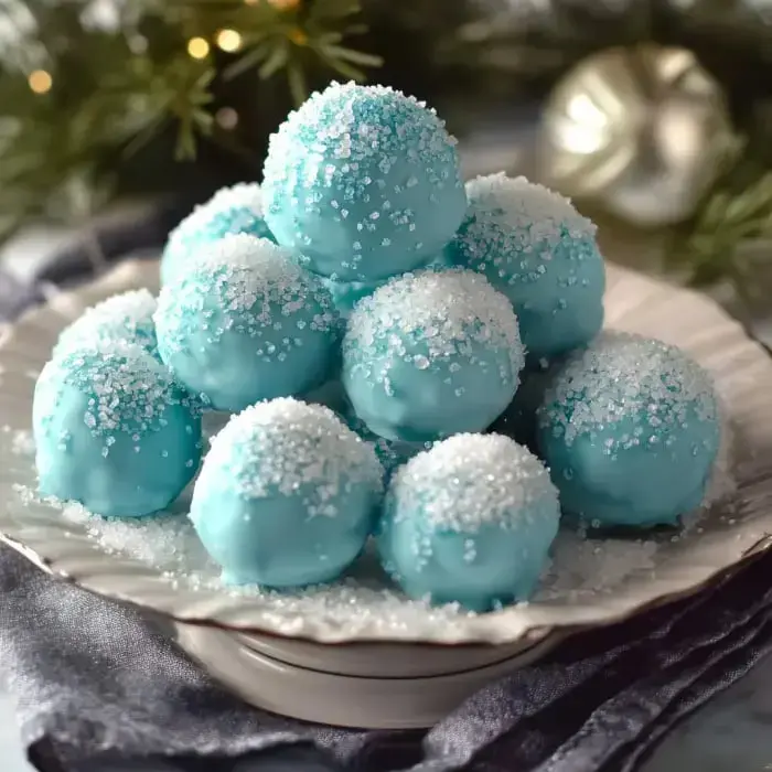 Sugar-coated blue balls stacked on a plate surrounded by festive greens, giving off a frosted winter vibe.
