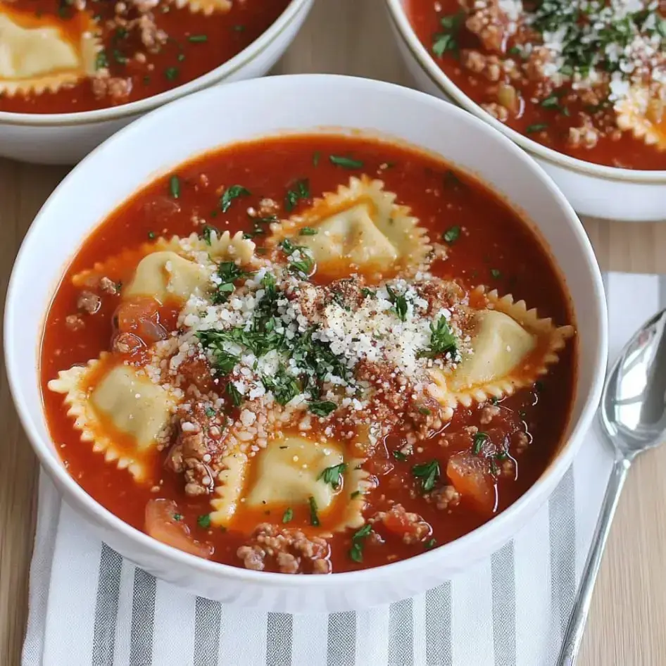 A hearty bowl filled with ravioli, meat, tomato broth, with parsley and cheese sprinkled on top.