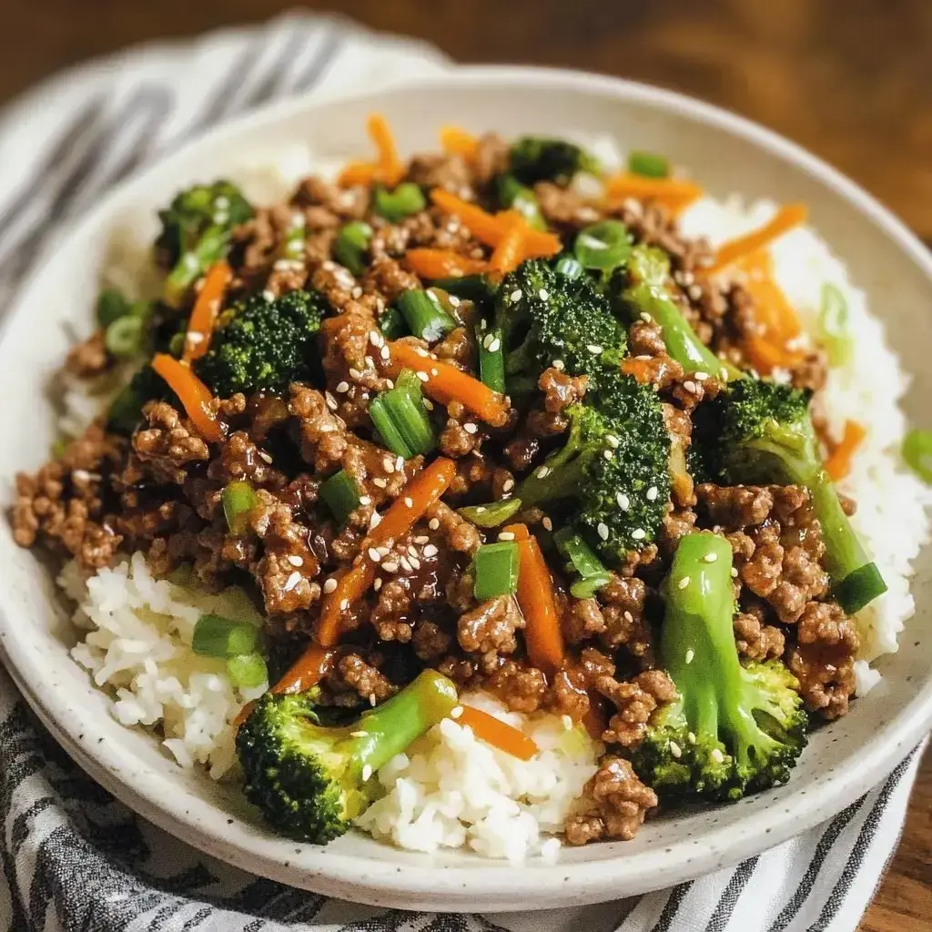 Rice topped with stir-fried beef, broccoli, carrots, and green onions with sesame seed garnish.