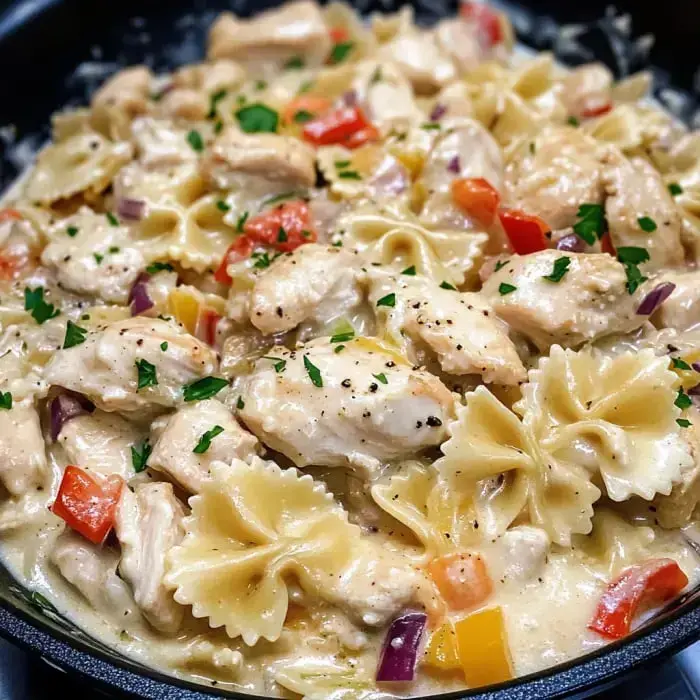 Close view of creamy chicken pasta with bow tie pasta, colorful veggies, and fresh parsley on top.
