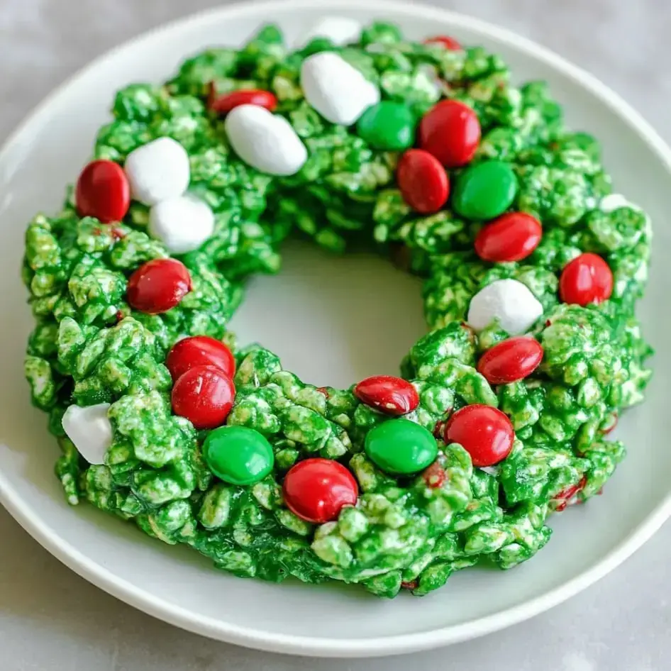 Round, green cornflake wreaths with red and green candy tucked in, white marshmallow dots, all arranged on a plate.
