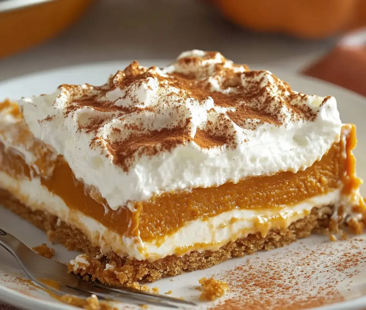 Pumpkin dessert slice with whipped cream and cookie base, topped with cinnamon sprinkles.