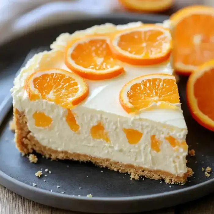 A thick slice of chilled orange cheesecake sits on a dark plate, topped with glossy orange bits.