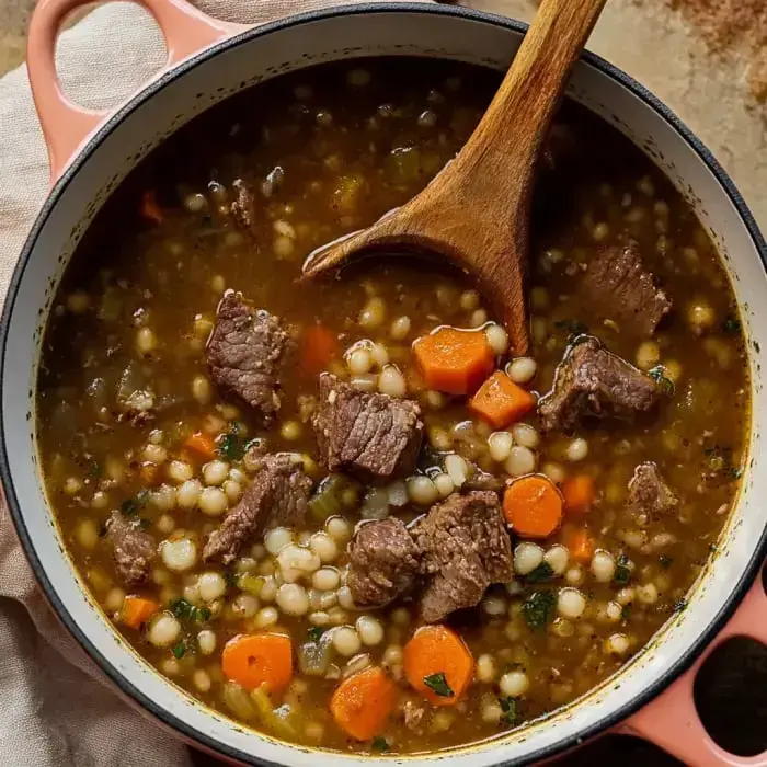 A wooden spoon stirring a hearty beef mixture with orange carrots and white pearl couscous in a cooking pot.