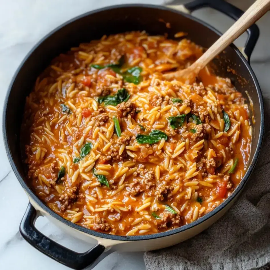 A steaming pot filled with creamy orzo, ground beef, fresh spinach and tomato sauce ready to serve.