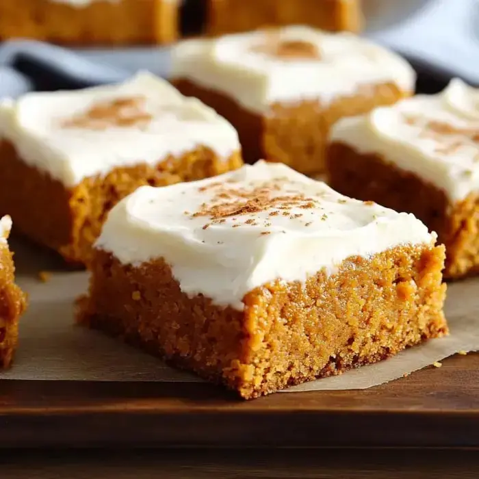 Frosted pumpkin bars with cinnamon on top, all lined up on a rustic cutting board.