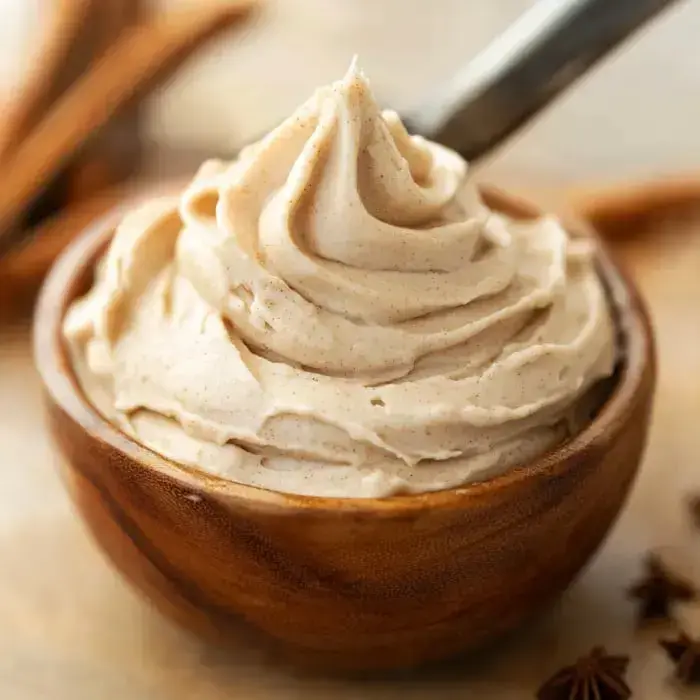 Smooth, light brown frosting swirled in a wooden bowl, each cinnamon stick cozied up nearby.
