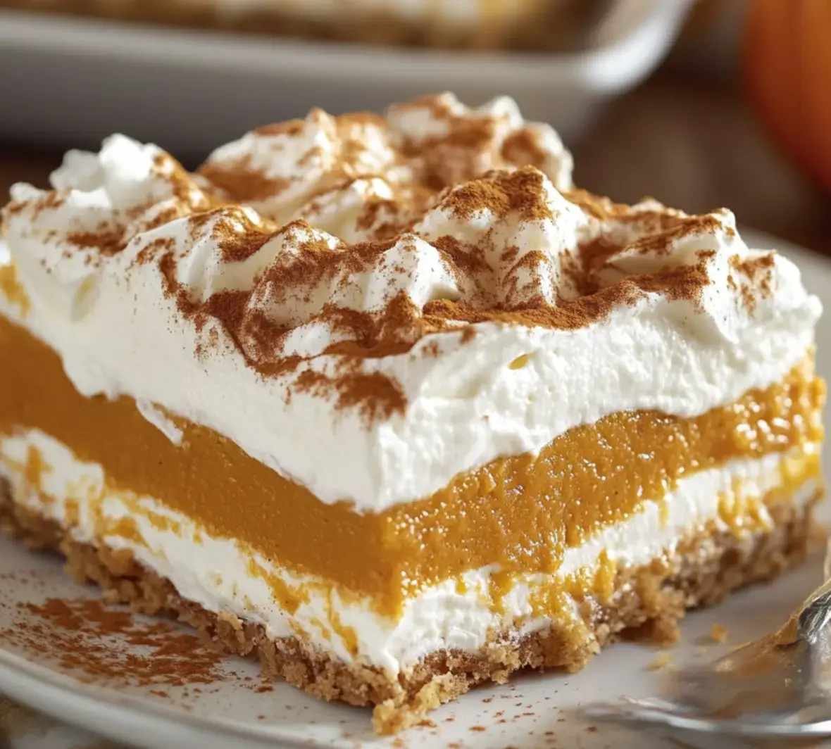 Close view of pumpkin dessert layered up with cream, a spiced crust, and a sprinkle of cinnamon and nuts.