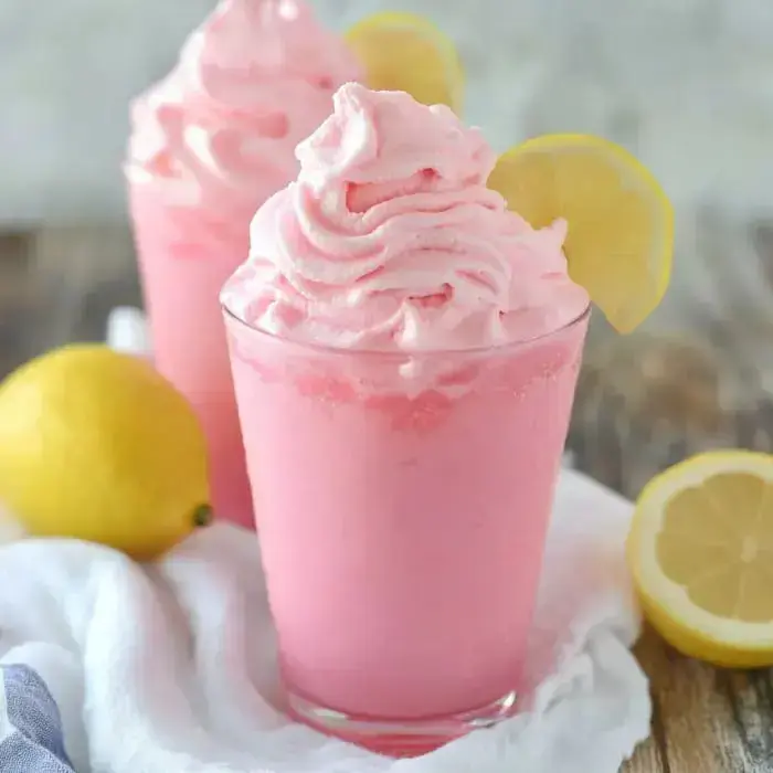 Pink lemonade drinks in glasses with lemon wedges and fresh lemons on a soft towel.