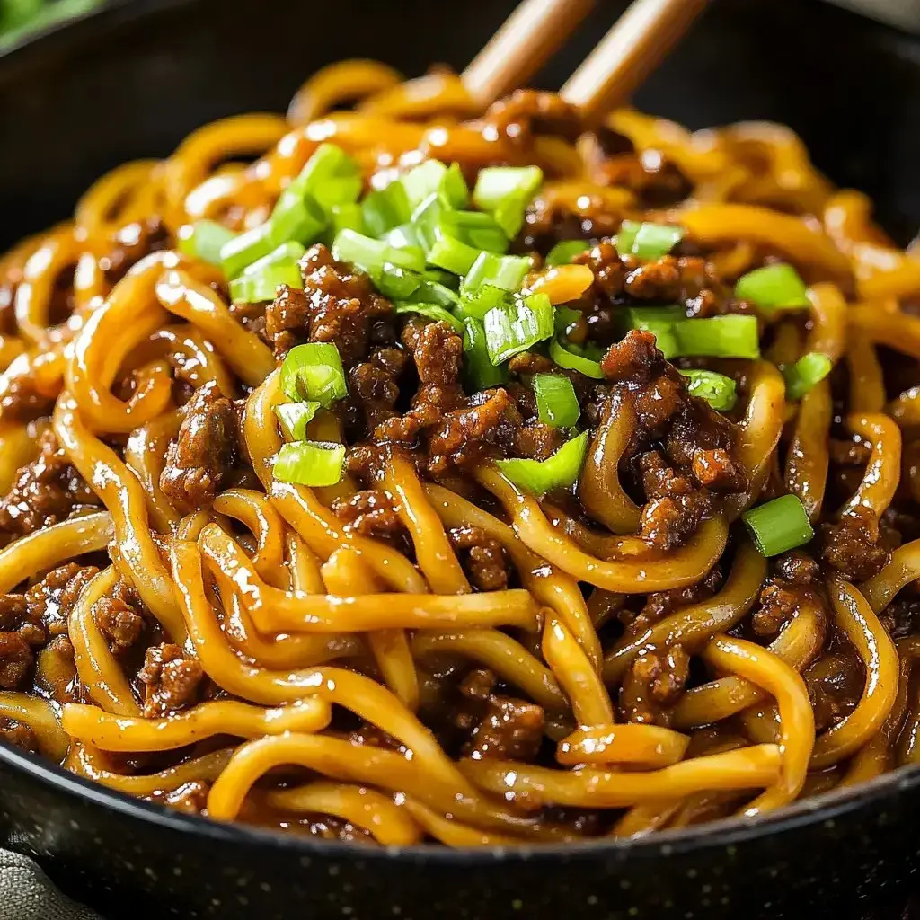 A bowl piled high with noodles, ground beef, and green onion scattered all over.