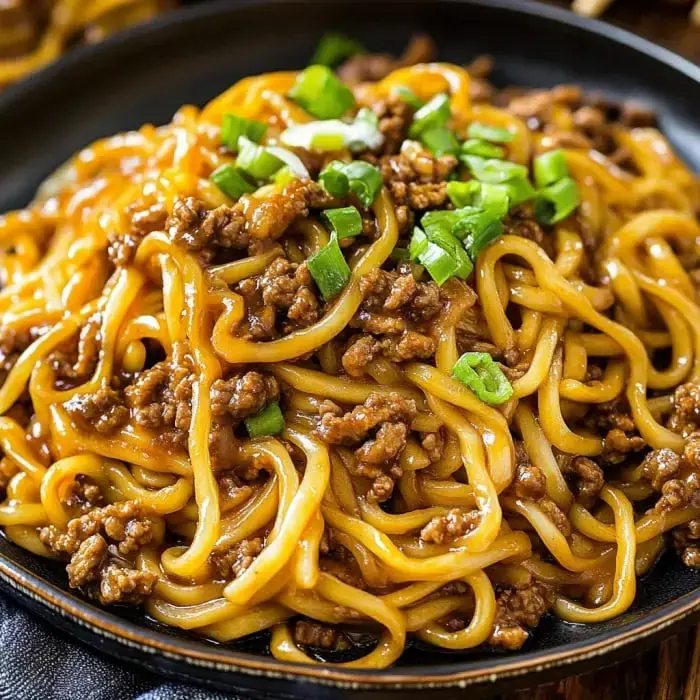 A plate showing noodles with ground beef and plenty of green onions on top.