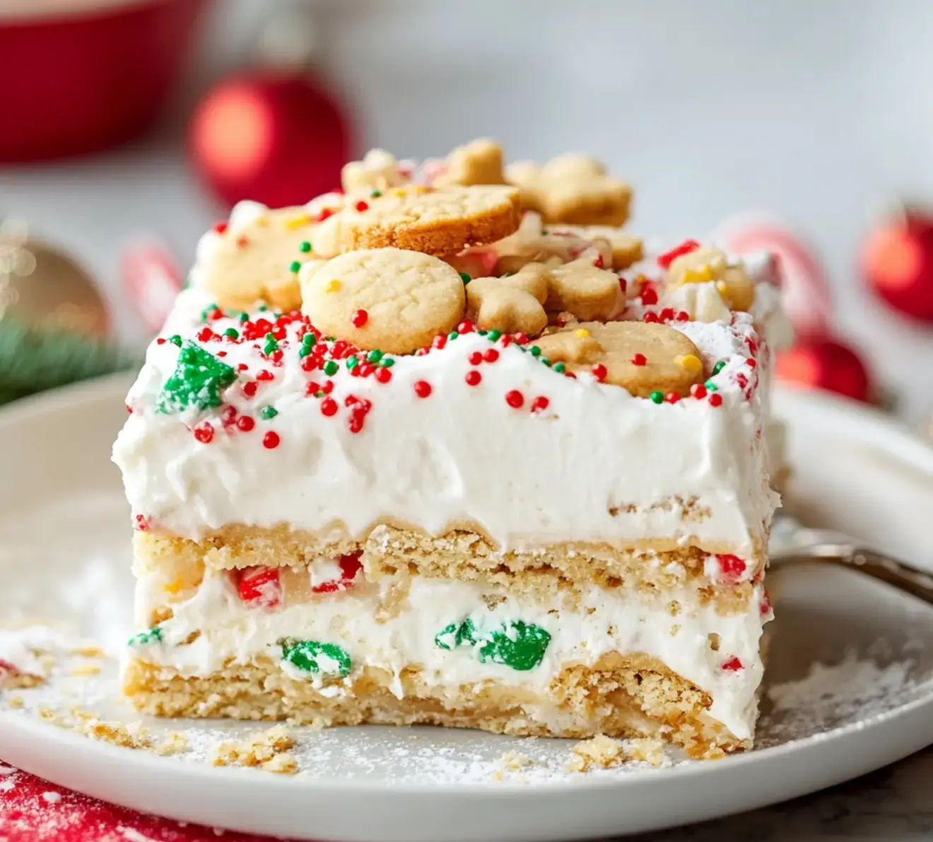 A plate shows a festive layered cake covered in whipped cream, colorful sprinkles, and cute cookie cutouts for holiday flair.