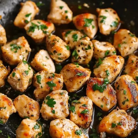 Pan-fried chicken pieces topped with fresh parsley in a skillet.
