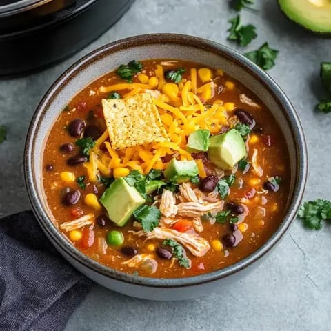 A cozy bowl filled with chicken, black beans, corn, tortilla chips, cheese, avocado, and cilantro.
