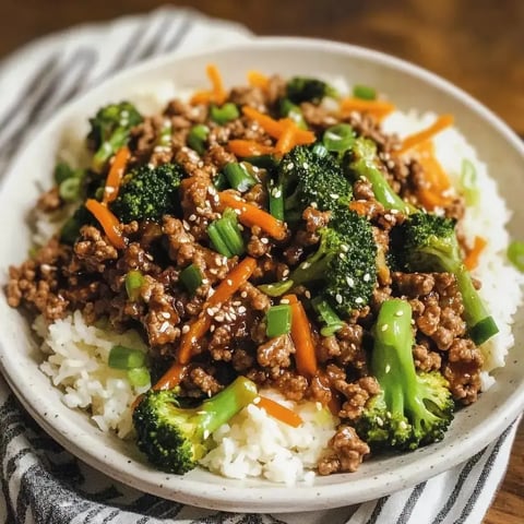 Rice topped with stir-fried beef, broccoli, carrots, and green onions with sesame seed garnish.