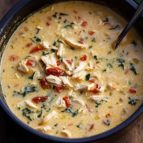 Creamy soup in a bowl topped with sun-dried tomatoes, chicken, and spinach.