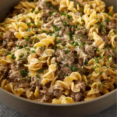 A bowl of beef stroganoff with noodles and green herbs.