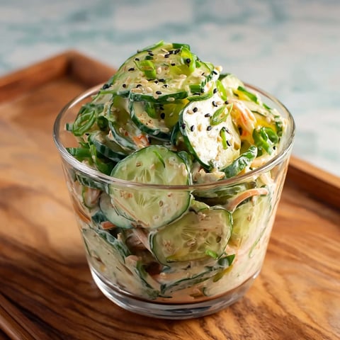 A glass bowl filled with a creamy Asian cucumber salad.